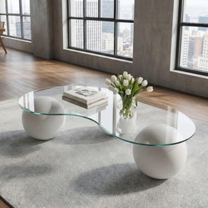 Könnte beinhalten: Ein moderner Couchtisch aus Glas mit einem einzigartigen, geschwungenen Design. Der Tisch hat eine klare Glasplatte, die von zwei weißen, kugelförmigen Sockeln getragen wird. Eine Vase mit weißen Tulpen und ein Stapel Bücher liegen auf dem Tisch, der auf einem grauen Teppich steht.