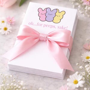 May include: A stack of white notepads wrapped with a pink satin ribbon. The top notepad features a graphic of three cartoon marshmallow bunnies in pink, purple, and yellow, with the text "oh...for peeps, sake!"