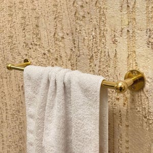 May include: A gold-coloured towel rail with a white towel hanging from it. The rail is mounted on a textured, beige wall. The towel is folded over the rail.