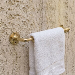 May include: A brass towel rail fixed to a textured wall, holding a folded white towel. The rail has a curved design with decorative detailing. The wall has a rough, stucco-like finish.