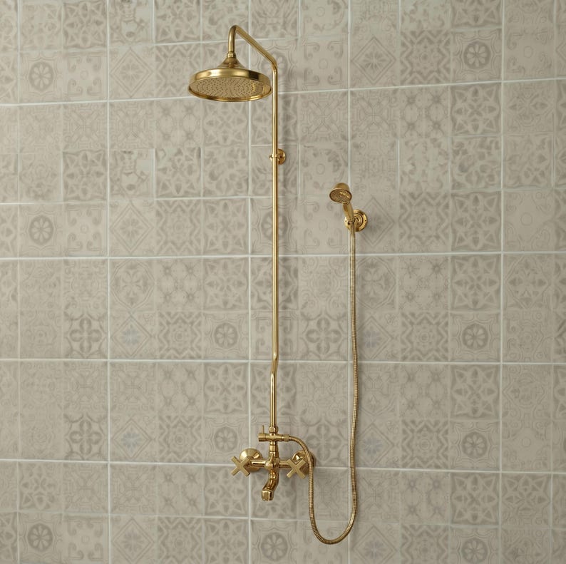 May include: A gold-toned shower system featuring a round overhead shower head, a vertical pipe, a handheld shower head attached by a flexible hose, and a wall-mounted faucet with two cross-style handles for controlling water flow and temperature.