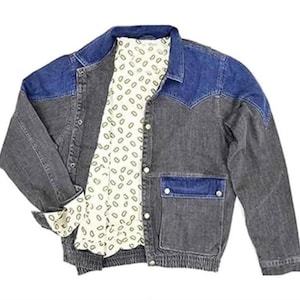 Puede incluir: Chaqueta vaquera de dos tonos. Los hombros y el cuello son de un azul más claro, contrastando con el cuerpo gris oscuro. Cuenta con un forro estampado color crema y dos bolsillos delanteros. Los puños están doblados.