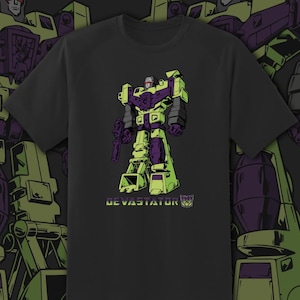 May include: Black t-shirt featuring a cartoon illustration of a robot character in shades of green, purple, and black. The word "DEVASTATOR" is printed in green below the robot, along with a logo.
