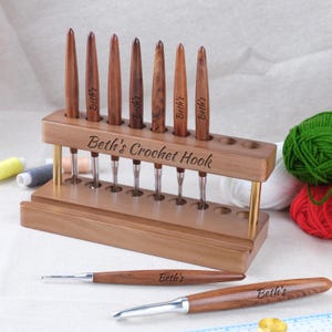 以下が含まれることがあります： 木製のかぎ針ホルダーと8つの木製かぎ針。 ホルダーには「Beth's Crochet Hook」と刻印されており、金色の金属製のサポートが付いています。 ホルダーの前には、それぞれ「Beth's」と刻印された2つの追加のかぎ針が置かれています。