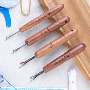 以下が含まれることがあります： 名前が刻まれた木製のシームリッパー4本。各リッパーは銀色の刃と赤い先端が付いています。Jessica、Cindy、Emily、Alina's Mimiの名前が茶色のハンドルに見えます。裁縫道具。