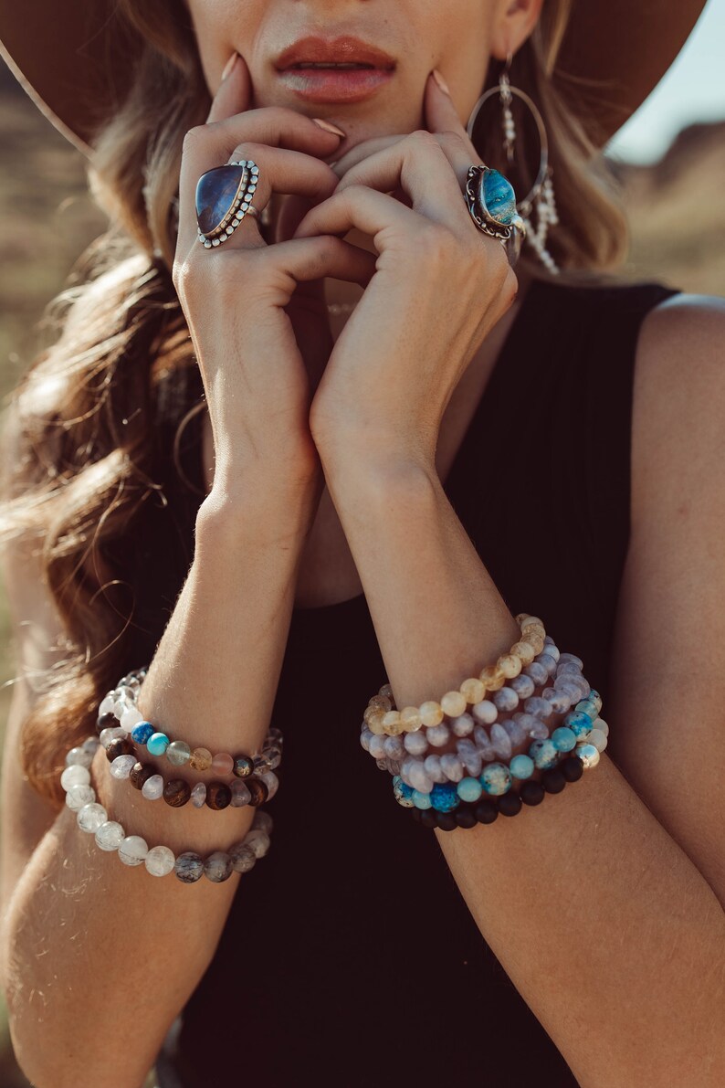 May include: A woman wearing a brown hat and a black top with multiple bracelets made of different colored stones. The bracelets are stacked on her wrist.