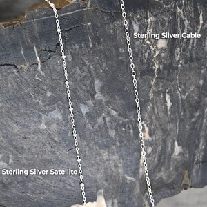 May include: Two sterling silver chains on a gray textured background. The chain on the left is a satellite chain and the chain on the right is a cable chain. The text "Sterling Silver Satellite" is below the left chain and the text "Sterling Silver Cable" is above the right chain.