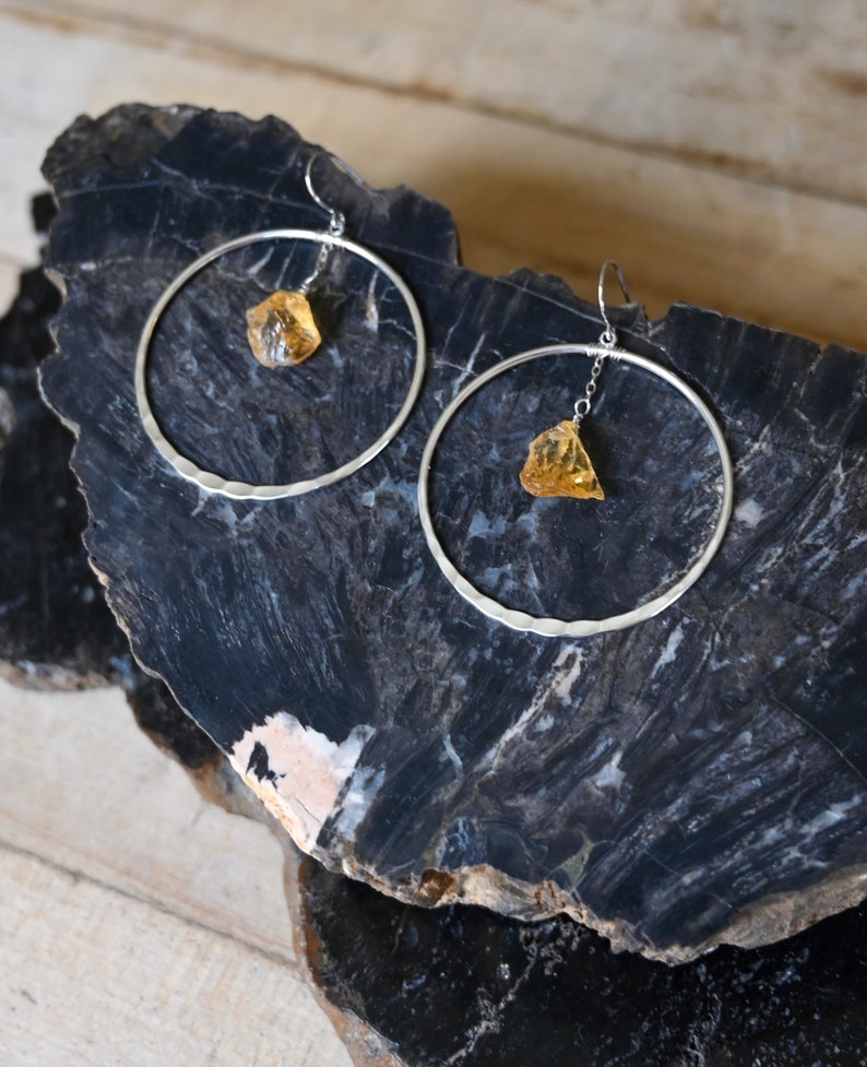 May include: A pair of silver hoop earrings with a dangling amber stone on each earring.
