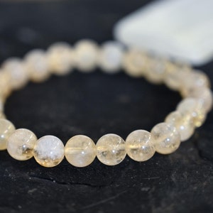 May include: A bracelet made of clear, light yellow, round beads. The beads are translucent and have a slight sparkle.