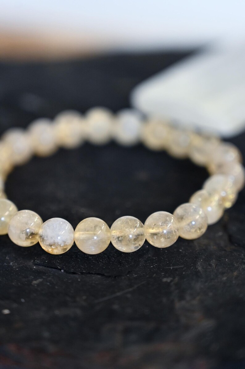 May include: A bracelet made of clear, light yellow, round beads. The beads are translucent and have a slight sparkle.