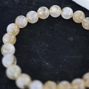 May include: A bracelet made of light brown and clear round beads. The beads are strung together on a clear elastic cord.