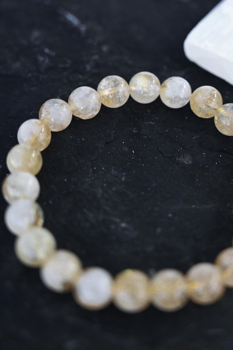 May include: A bracelet made of light brown and clear round beads. The beads are strung together on a clear elastic cord.