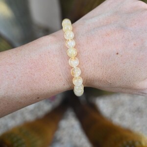 May include: A yellow citrine gemstone bracelet with round beads. The bracelet is on a person's wrist.
