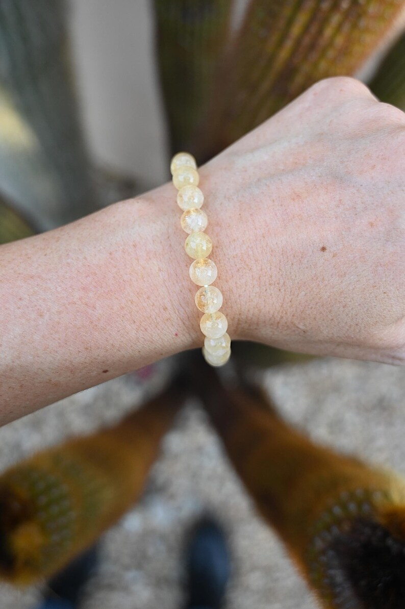 May include: A yellow citrine gemstone bracelet with round beads. The bracelet is on a person's wrist.
