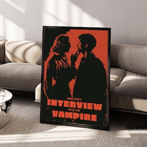 Puede incluir: Un póster rectangular enmarcado con una ilustración gráfica de alto contraste en negro y naranja de dos figuras frente a frente. El texto ANNE RICE'S INTERVIEW WITH THE VAMPIRE aparece en letras mayúsculas naranjas sobre un fondo negro.