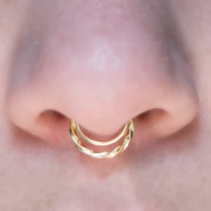 Puede incluir: Primer plano de un piercing en la nariz con dos aros de oro. Los aros están retorcidos y entrelazados.