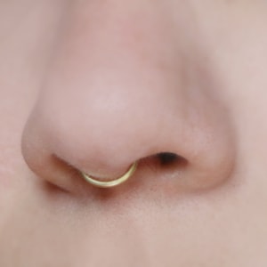 close up of human nose wearing a 14k gold peakabo septum cuff  by Curly Cuffs