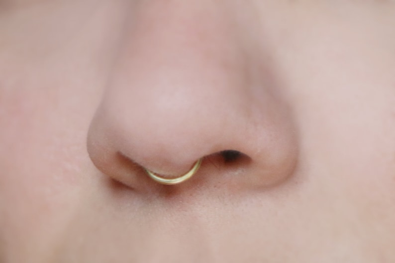 close up of human nose wearing a 14k gold peakabo septum cuff  by Curly Cuffs