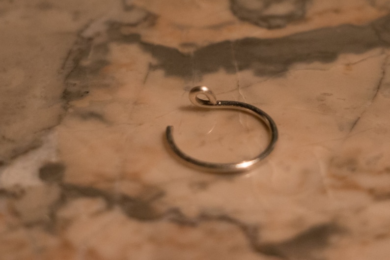 Puede incluir: Un aro de nariz de plata con un aro peque&ntilde;o y una abertura curva.