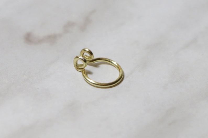 close up of shiny gold septum cuff laying on a white marble background. Two curly ends allow for comfortable wear