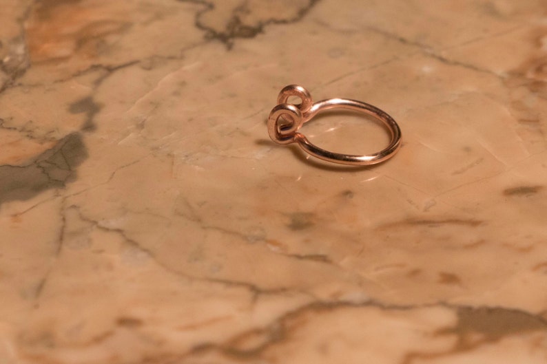May include: A rose gold nose ring with a double loop design.