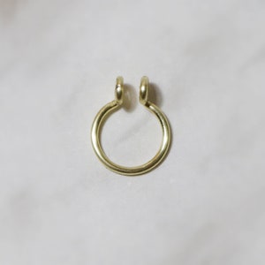 close up of shiny gold septum cuff laying on a white marble background. Two curly ends allow for comfortable wear