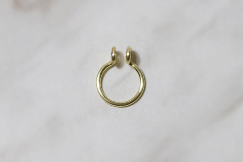 close up of shiny gold septum cuff laying on a white marble background. Two curly ends allow for comfortable wear