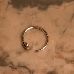 Puede incluir: Un aro para la nariz de plata con un dise&ntilde;o simple.
