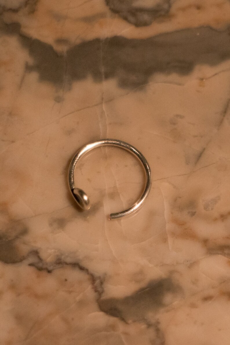 Puede incluir: Un aro para la nariz de plata con un dise&ntilde;o simple.