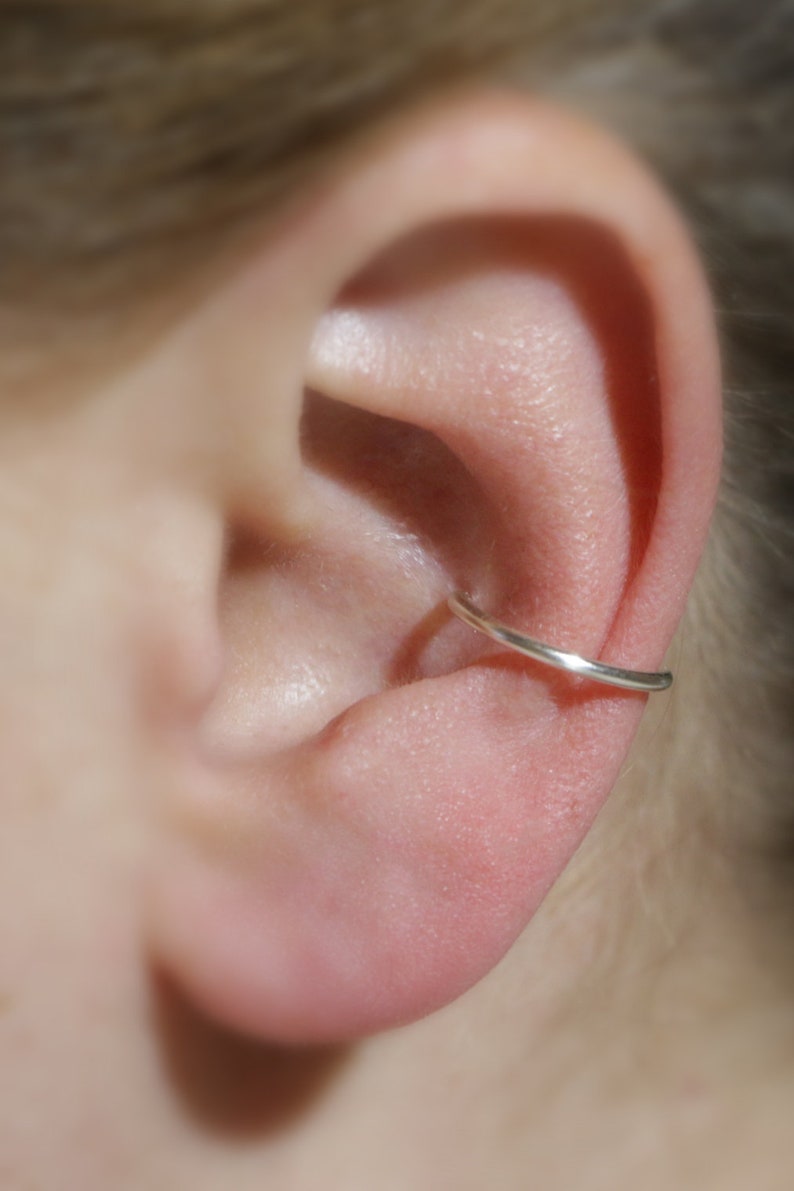 close up of a human ear wearing an ear cuff around their mid mid ear cartilage.