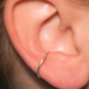 Puede incluir: Primer plano de una oreja con un peque&ntilde;o aro de plata. El arete est&aacute; en el l&oacute;bulo superior de la oreja.