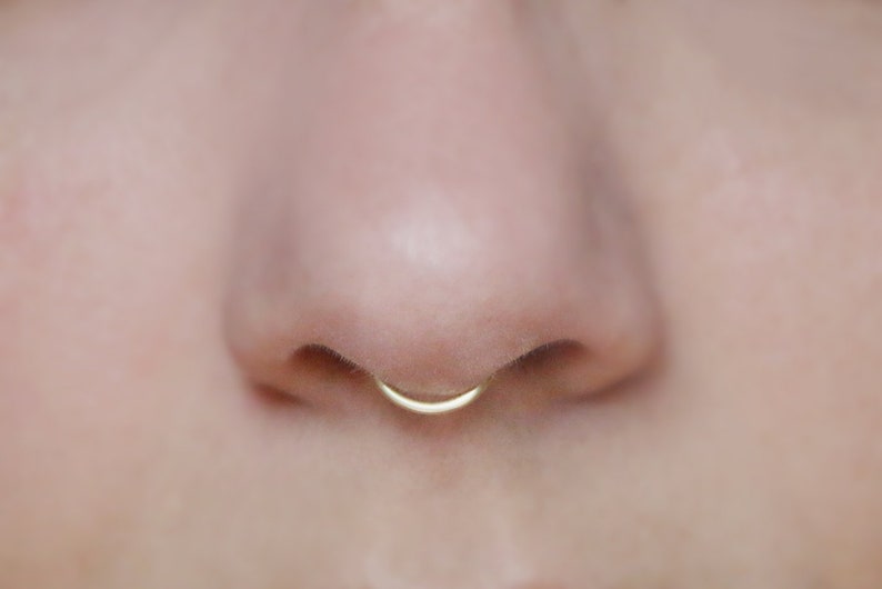 close up of human nose wearing a 14k gold peakabo septum cuff  by Curly Cuffs