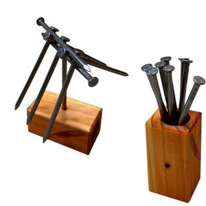 May include: Two wooden nail holders. One holds nails upright, the other has nails angled. The wood is light brown. The nails are silver and have rounded heads. The background is white.