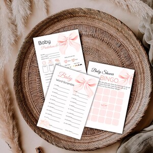May include: Three baby shower game cards with pink bow illustrations. The cards include "Baby Predictions & Advice", "Baby Word Scramble", and "Baby Shower Bingo" on a woven tray.