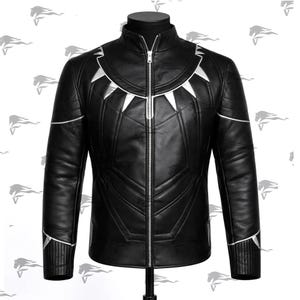 Puede incluir: Chaqueta de cuero negra con detalles plateados. La chaqueta presenta un cuello alto, una cremallera completa y diseños geométricos plateados en el pecho y los hombros. Las mangas tienen ribetes plateados en los puños. La chaqueta se exhibe en un maniquí negro.