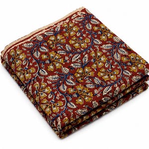 Könnte beinhalten: Ein gefaltetes Stück Stoff mit einem tiefroten Hintergrund und einem sich wiederholenden Blumenmuster in Gelb, Weiß und Blau. Das Textil zeigt komplizierte botanische Motive, einschließlich stilisierter Blumen und Blätter auf der gesamten Oberfläche.