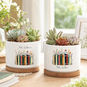 May include: Two white ceramic cylindrical planters with bamboo saucers, each containing assorted succulents. The planters feature a colorful graphic of a row of books topped with wildflowers and the personalized text Mrs. Wilson.
