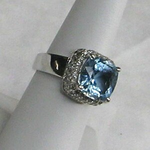 May include: A silver ring with a large, square-shaped blue gemstone surrounded by smaller, clear gemstones.