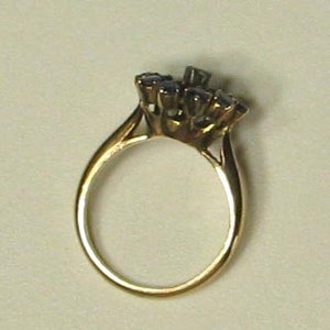 Pode incluir: Um anel de ouro com um grupo de pedras preciosas azuis engastadas em garras.