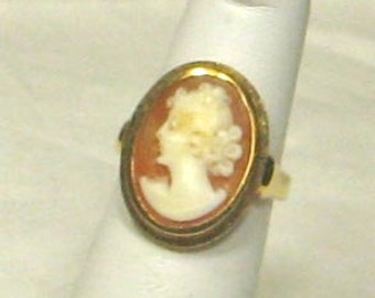 May include: A gold-toned ring with a cameo featuring a woman's profile in white on a brown background.