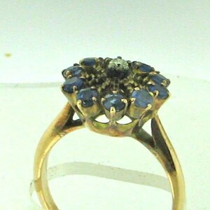Pode incluir: Um anel de ouro com um grupo de safiras azuis e um &uacute;nico diamante no centro.