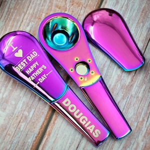 Könnte beinhalten: Drei schillernde, lila-blaue Metallpfeifen werden auf einer Holzoberfläche gezeigt. Eine Pfeife ist mit "I ❤️ BEST DAD HAPPY FATHER'S DAY" graviert und eine andere mit dem Namen "DOUGLAS". Die Pfeifen haben ein schlankes, modernes Design.