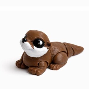 May include: A brown otter figurine with a white chest and black eyes. The otter is lying down, with its paws and tail visible. The figurine is made of a smooth material and is set against a white background.