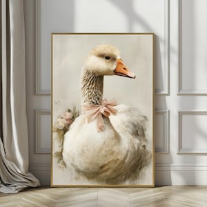 May include: A framed artwork featuring a goose with white feathers, a beige head, and an orange beak. The goose wears a pink bow around its neck and is surrounded by soft pink flowers. The artwork has a gold frame and is displayed against a neutral background.
