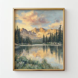 May include: A framed landscape painting depicts a serene mountain lake scene. The artwork features a golden-hued frame, a reflective lake, evergreen trees, and a mountain range under a sunset sky. The painting evokes a sense of tranquility and natural beauty.