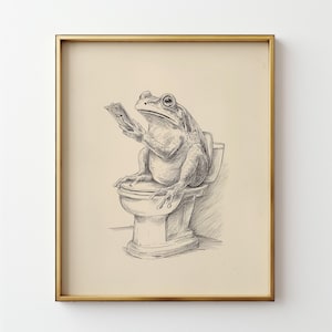 May include: A framed pen and ink illustration depicts a frog sitting on a toilet, engrossed in reading. The artwork is in black and white, with a gold-colored frame. The frog is the central focus of this humorous art piece.