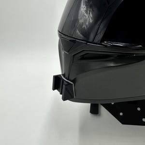 May include: A black motorcycle helmet with a glossy finish. The helmet has a sleek, aerodynamic design with a dark visor and a chin strap. The helmet is designed for safety and protection.