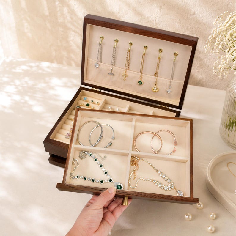 May include: A dark wood jewelry box with multiple compartments and drawers, showcasing various necklaces, bracelets, and rings. The box is open, revealing the organized storage of the jewelry pieces. The interior is lined with a light-colored fabric.