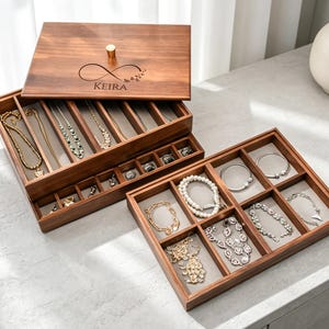 May include: A wooden jewelry box with multiple compartments, filled with necklaces, bracelets, and rings. The box is open, revealing the organized storage. The lid is engraved with the name "Keira" and an infinity symbol.
