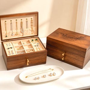May include: A wooden jewellery box with multiple compartments and drawers. The open box displays necklaces and rings. A white oval dish holds a necklace and earrings. The closed box has the name "Vivian" and the date "10.18.2025" engraved on the lid.